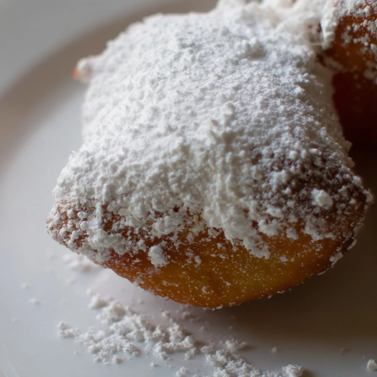 Close-up of freshly fried Mardi Gras beignets showcasing their crispy, golden edges and sweet, snowy powdered sugar coating.
