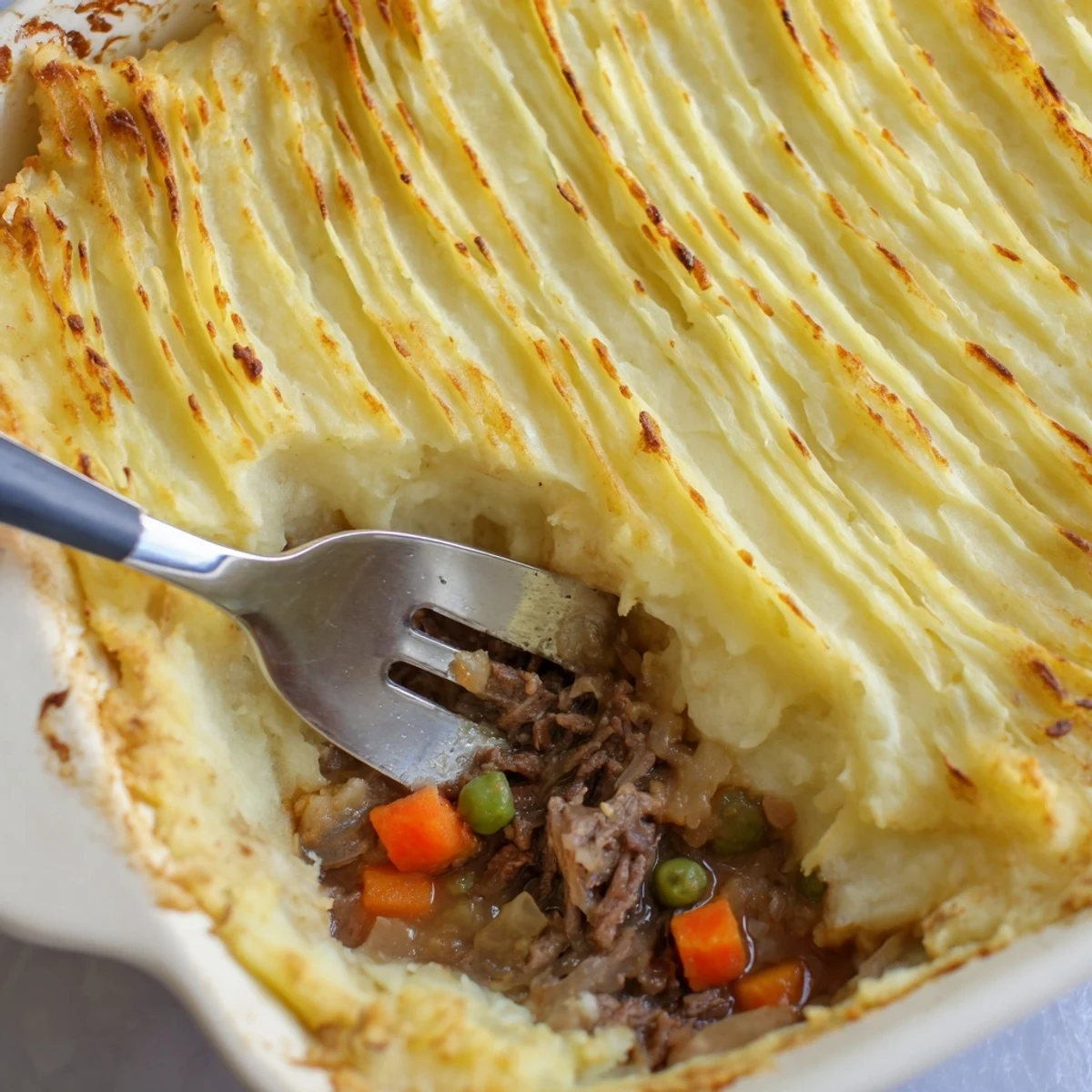 A close-up of Beef Shepherds Pie with Peas, featuring golden mashed potato ridges over savory beef and tender vegetable filling.  
