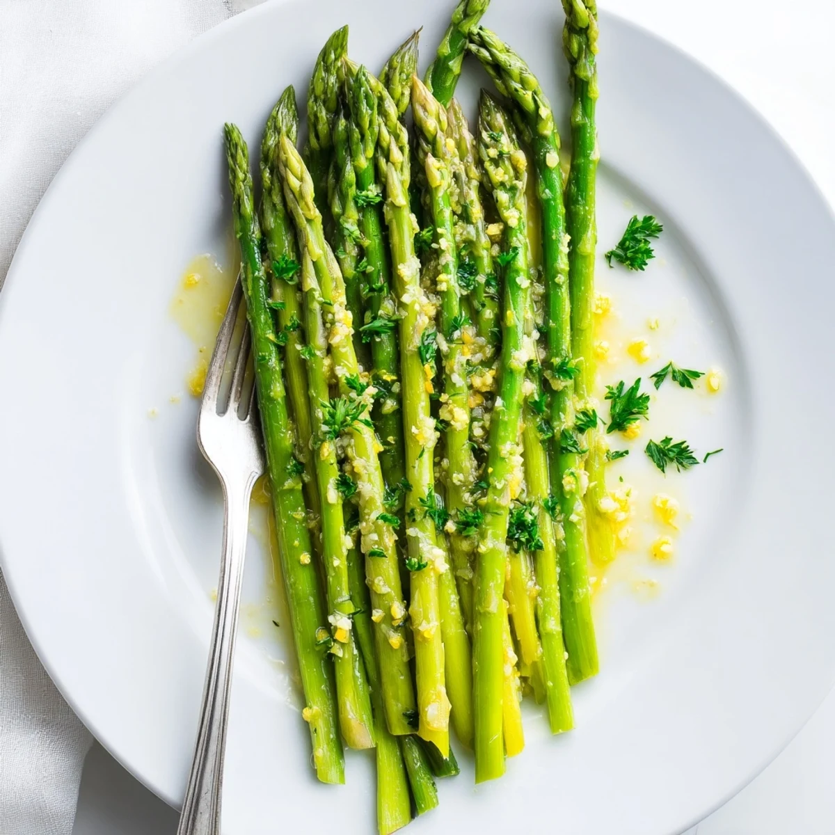 Freshly cooked Lemon Garlic Asparagus rests on a white plate, garnished with parsley, its buttery sheen and lemony aroma inviting a quick, easy dinner side.