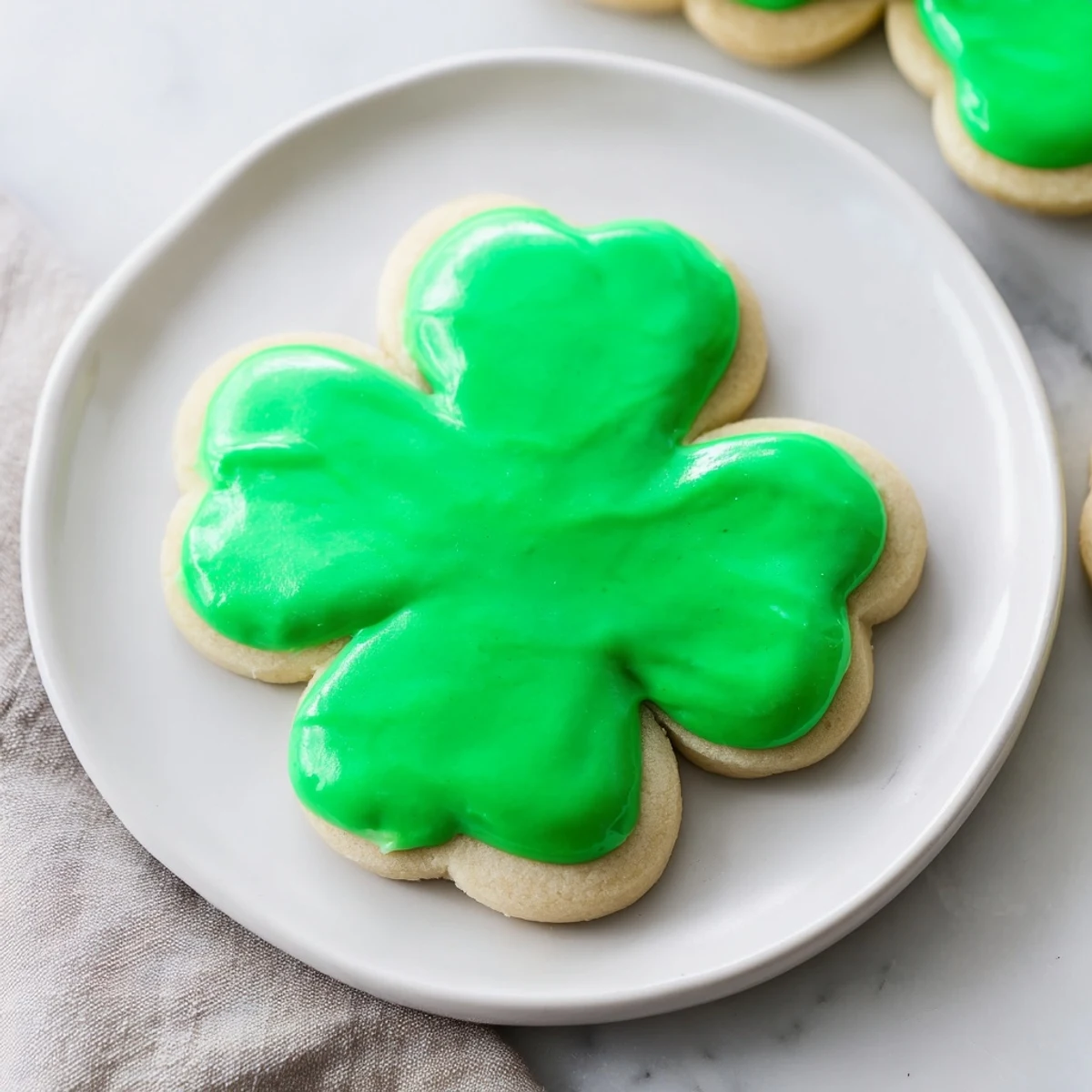 Four Shamrock Sugar Cookies with Green Icing sit on a marble surface, their delicate shapes and sweet aroma inviting celebration.