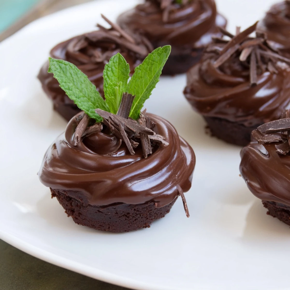 Freshly baked Mint Brownie Bites with glossy ganache and a mint leaf garnish on a wooden board.