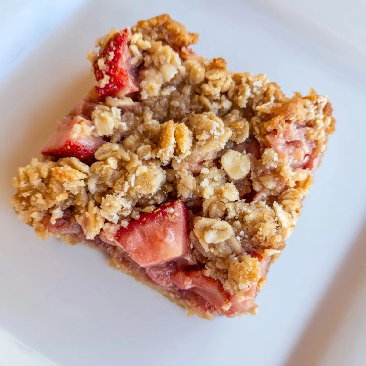 A close-up of a freshly baked Strawberry Rhubarb Crumble Bar cut into squares, revealing layers of sweet strawberries and tangy rhubarb.  