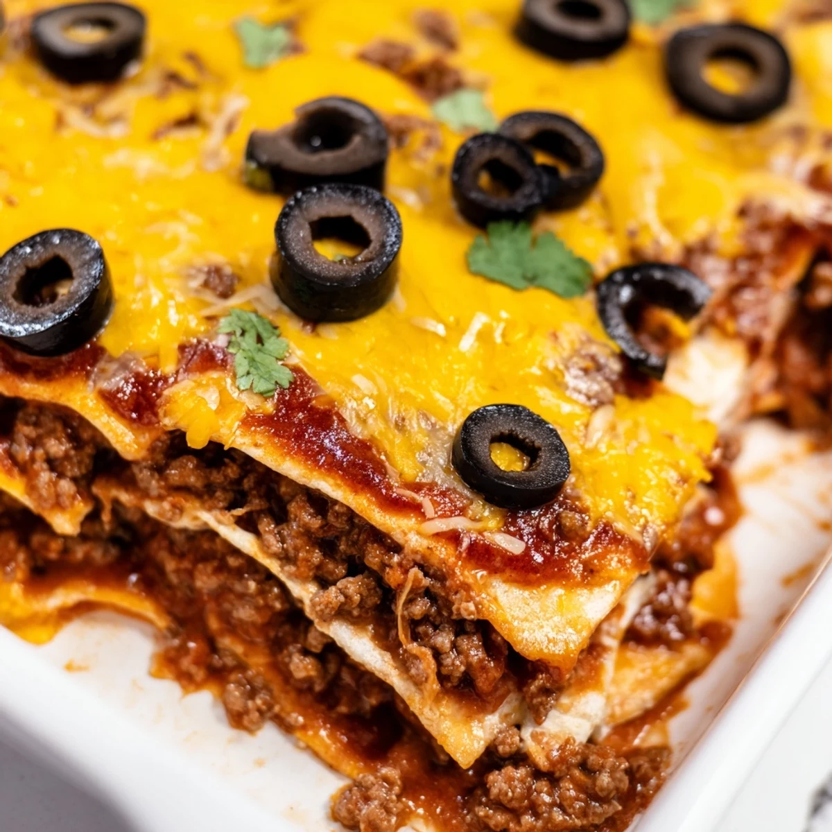 Fresh cilantro tops a slice of the Beef Enchilada Casserole, with a dollop of cool sour cream ready beside the saucy dish.