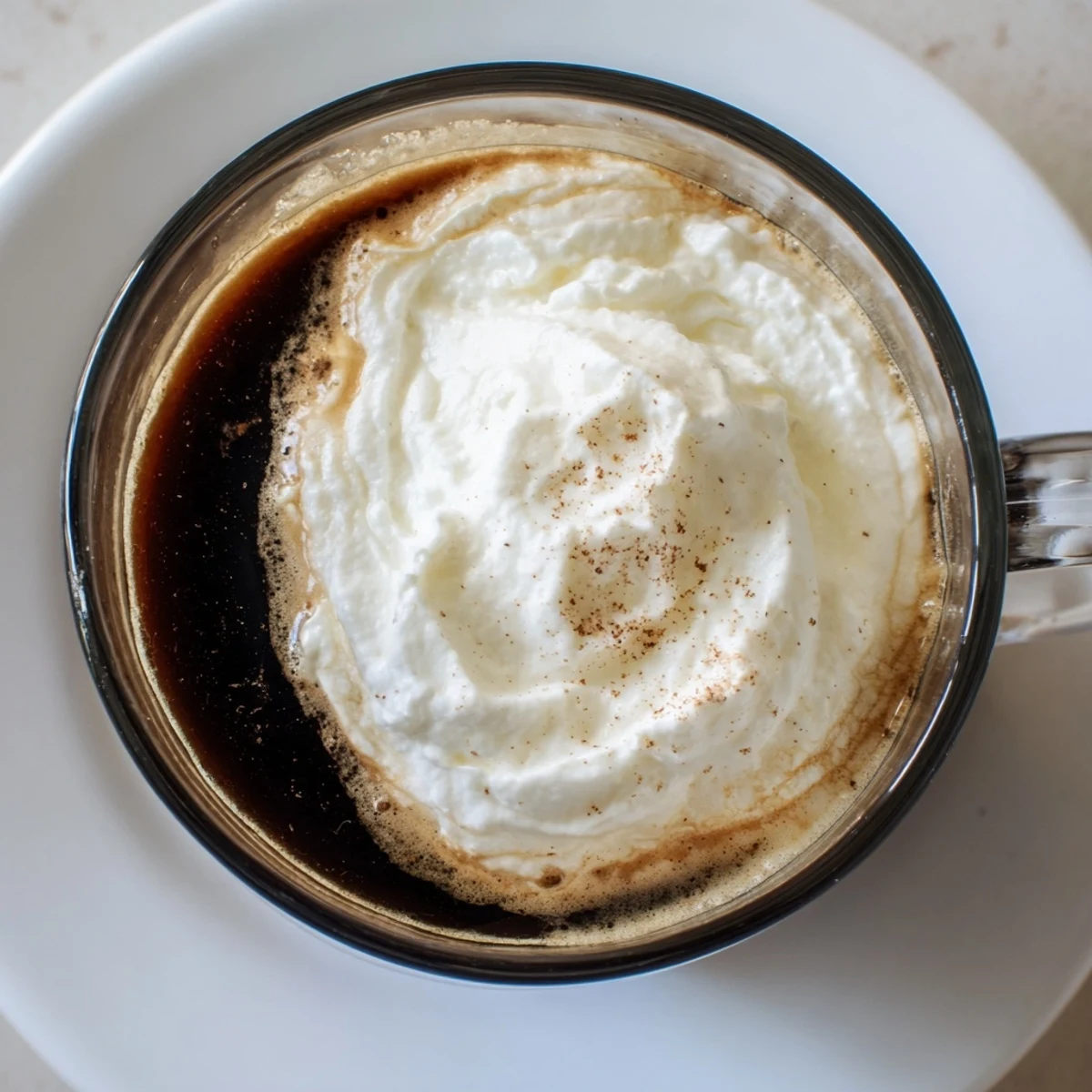 A close-up of a Irish Coffee Mocktail with Whipped Cream in a clear heatproof glass, showing the rich coffee and a fluffy, snowy topping.
