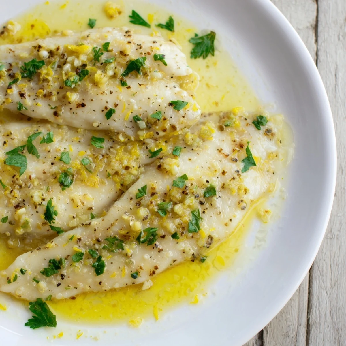 Golden baked tilapia fillets glistening with lemon butter sauce, garnished with fresh parsley.