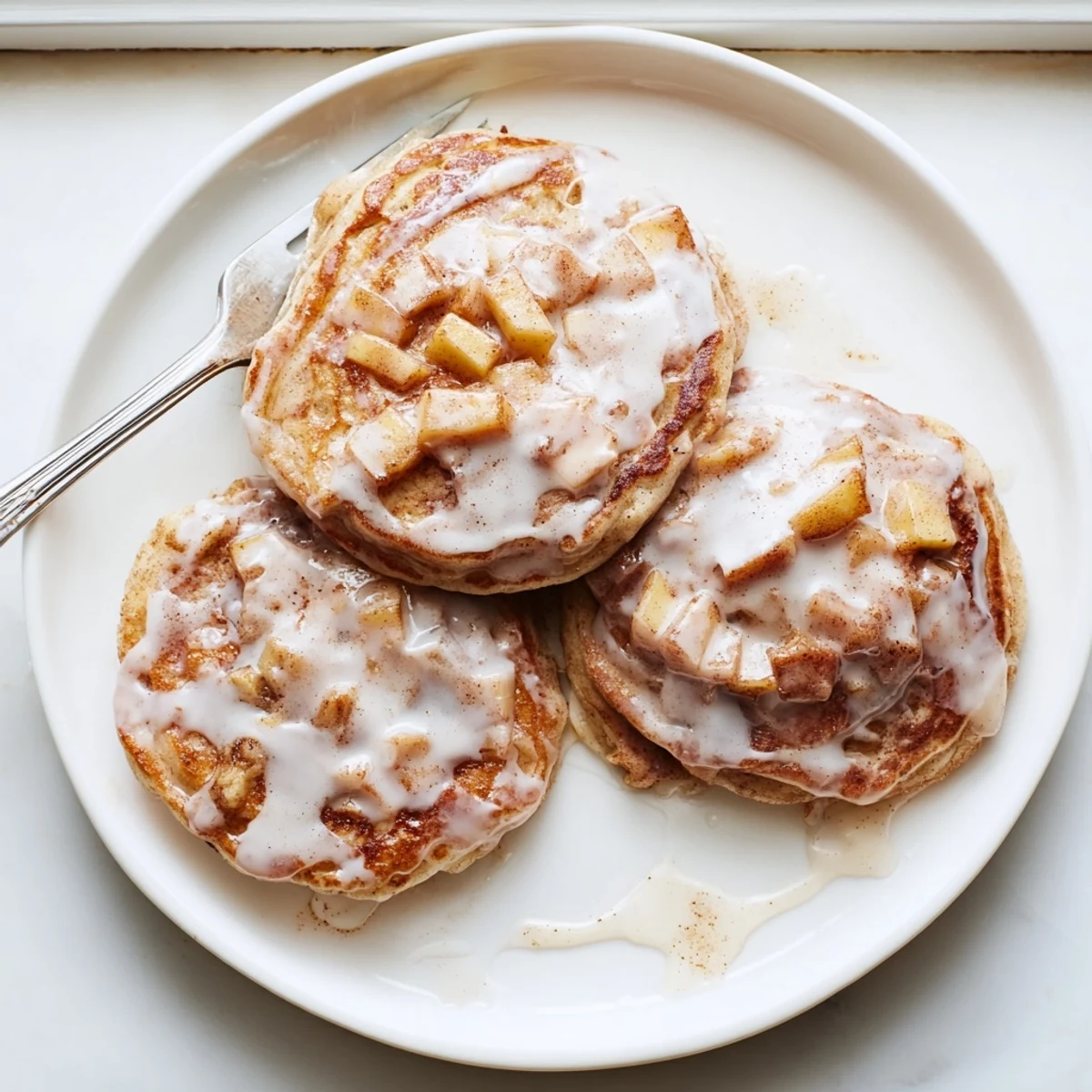 Golden Apple Fritter Pancakes stacked high, drizzled with sweet glaze, perfect for a cozy American breakfast.