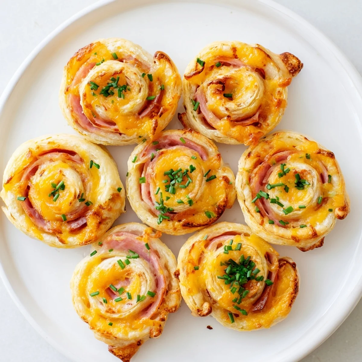 Golden baked Easter ham cheddar pinwheels arranged on a white serving platter with fresh parsley garnish
