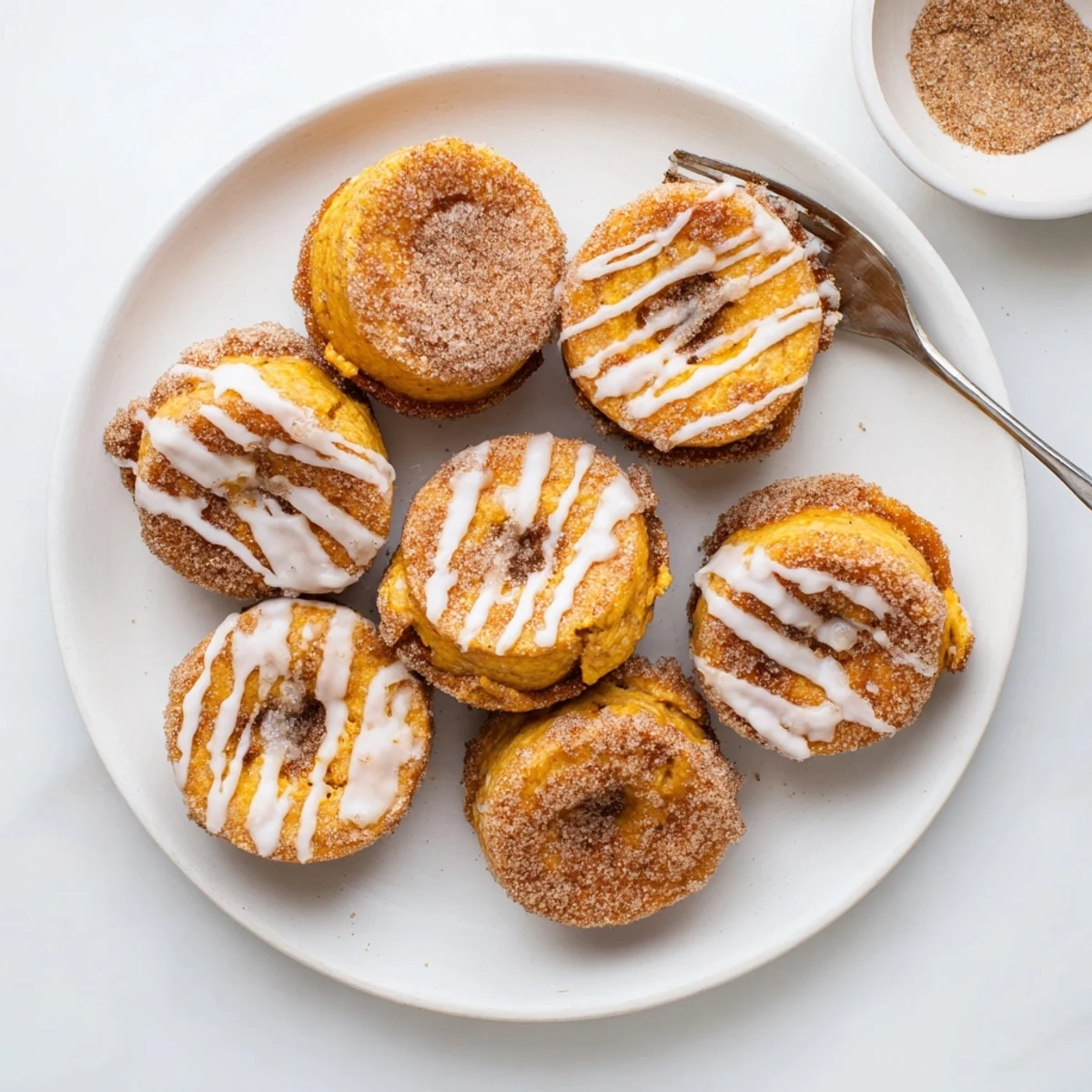 Golden brown pumpkin spice biscuit donuts coated in cinnamon sugar with sweet vanilla glaze drizzled on top