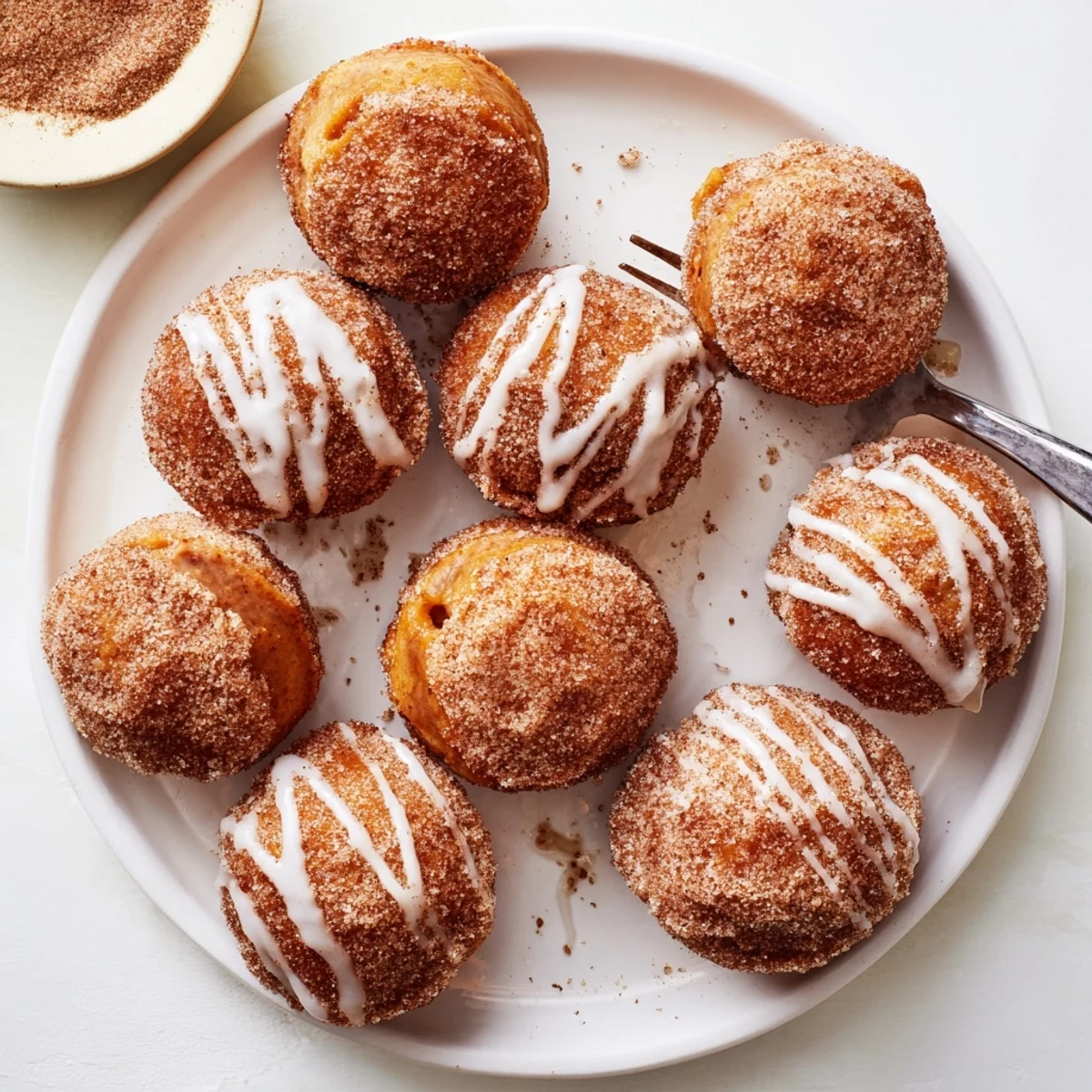 Soft fluffy pumpkin biscuit donuts stacked on a serving plate with white glaze and autumn spice garnish