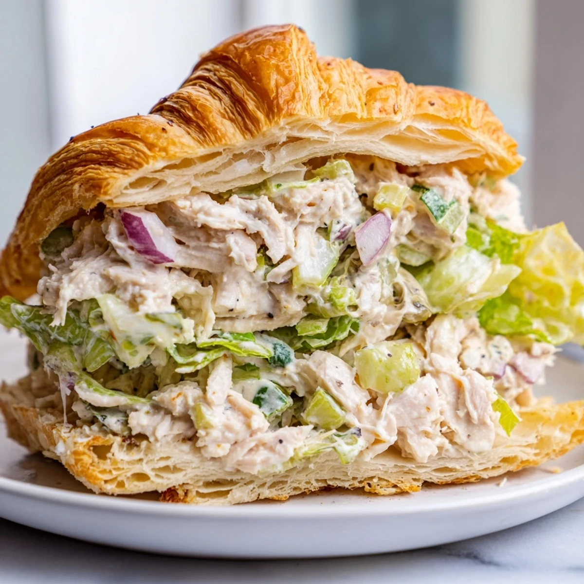 Golden flaky croissant stuffed with creamy chicken Caesar salad and crisp romaine lettuce