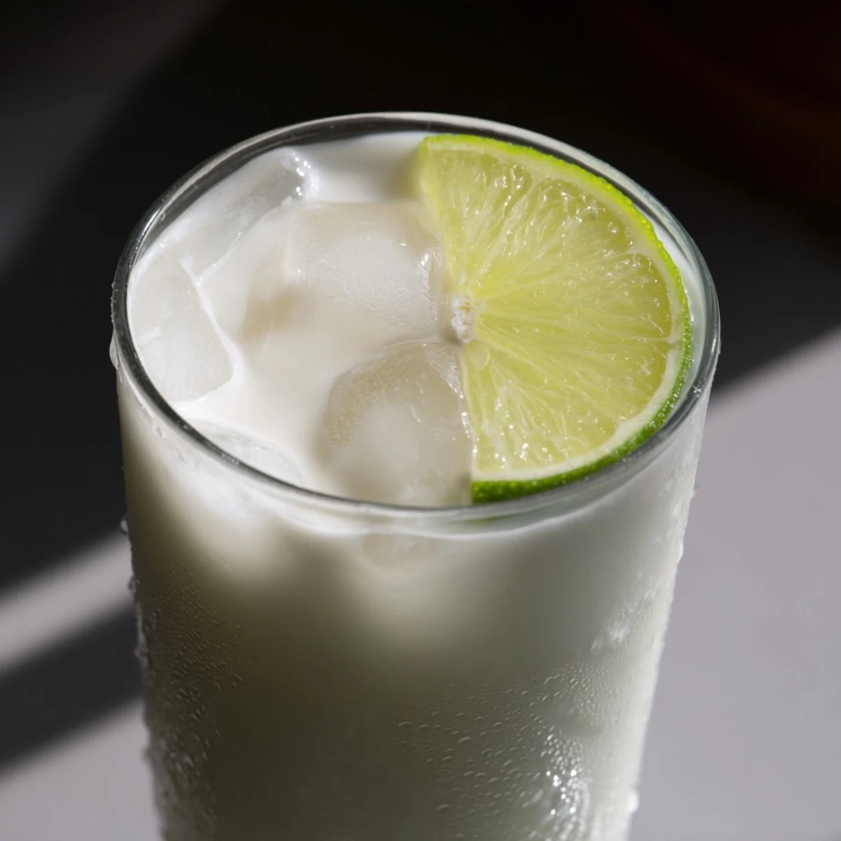 Light green creamy Brazilian lemonade in a clear glass with floating lime pulp and ice