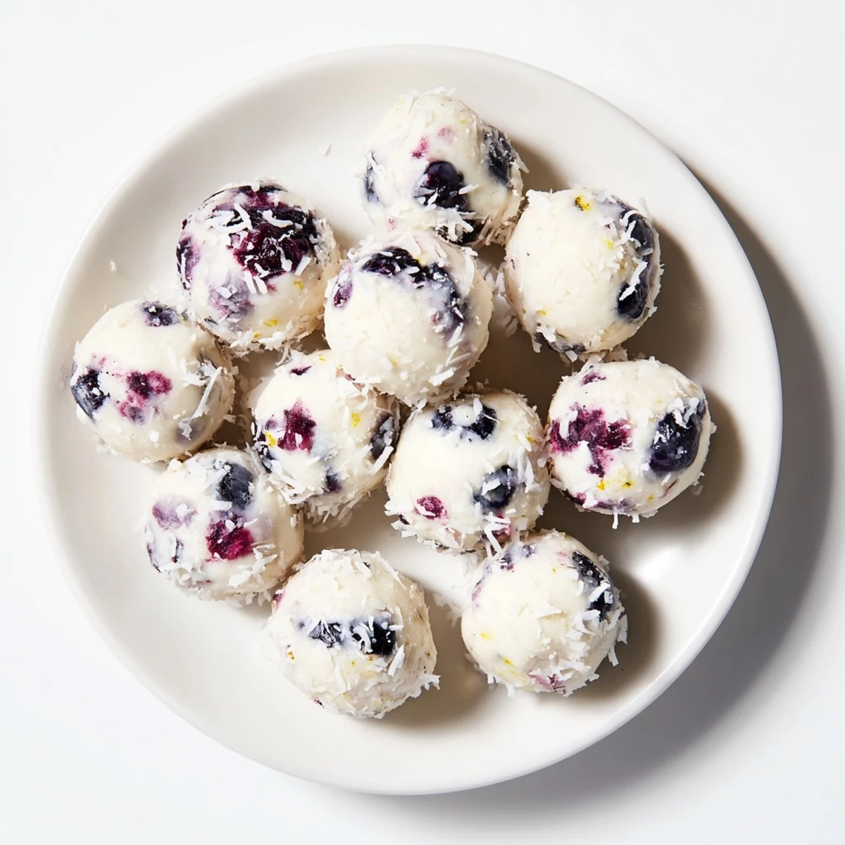 Creamy blueberry cheesecake protein bites rolled in coconut on a white plate