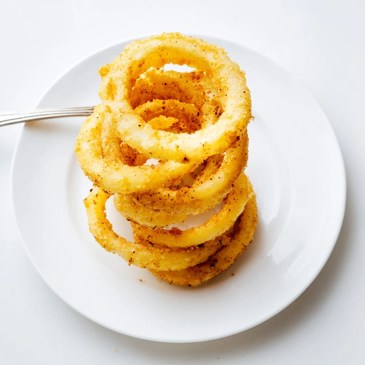 Heap of golden onion ring chips sprinkled with paprika alongside a creamy dipping sauce