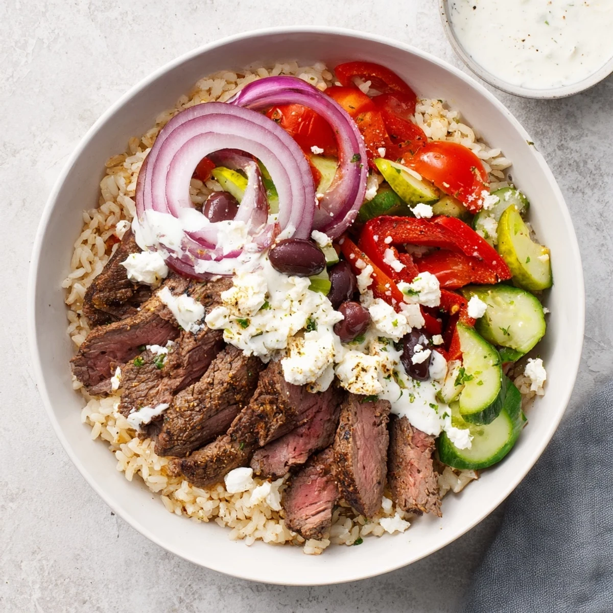Colorful Mediterranean steak bowl with grilled flank steak over herbed rice and fresh vegetables