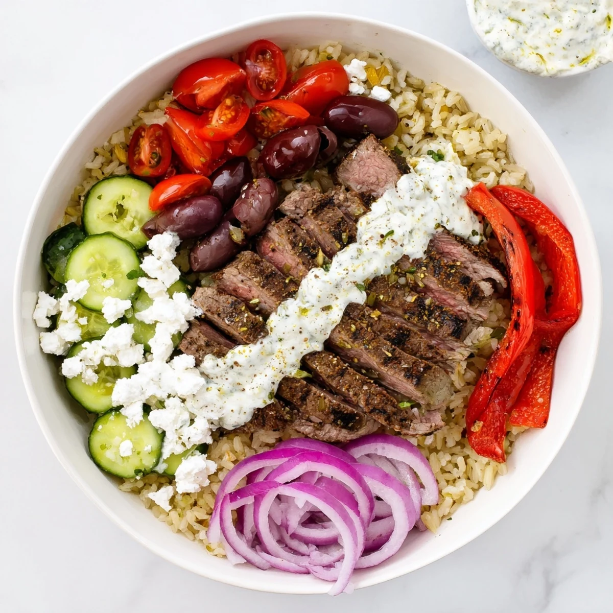 Protein-packed Mediterranean steak bowl featuring juicy sliced steak with feta and tangy yogurt sauce