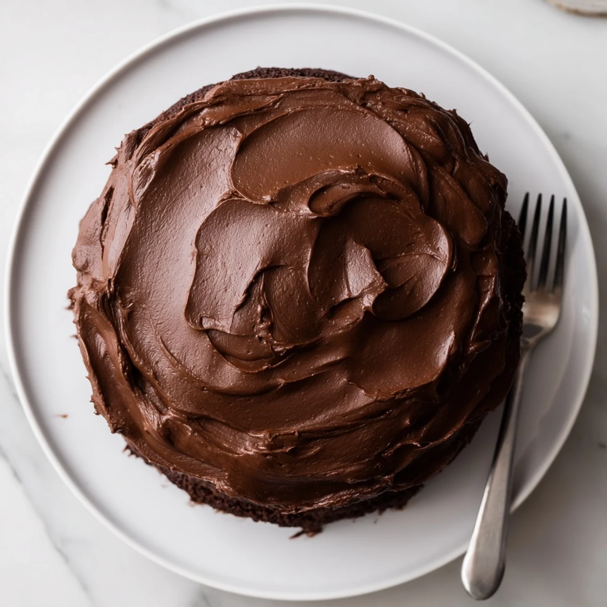 Decadent chocolate cake layered with rich silky frosting on a white serving plate