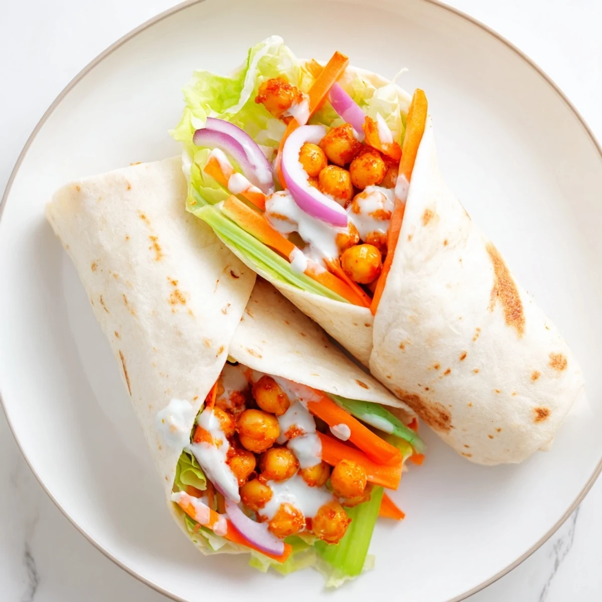 Vegetarian buffalo chickpea wrap with red onion, celery, and drizzled blue cheese dressing on a white plate