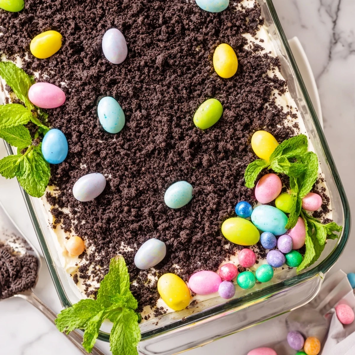 Easter dirt cake casserole with layers of creamy pudding topped with pastel candy eggs and chocolate cookie crumbs