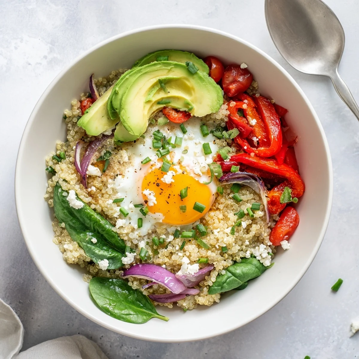 Hearty gluten-free savory quinoa breakfast bowl in white dish topped with runny egg avocado slices and chives