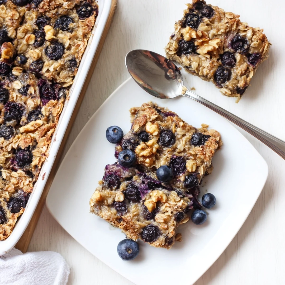 Fresh blueberry lemon baked oatmeal squares served warm in a white ceramic baking dish