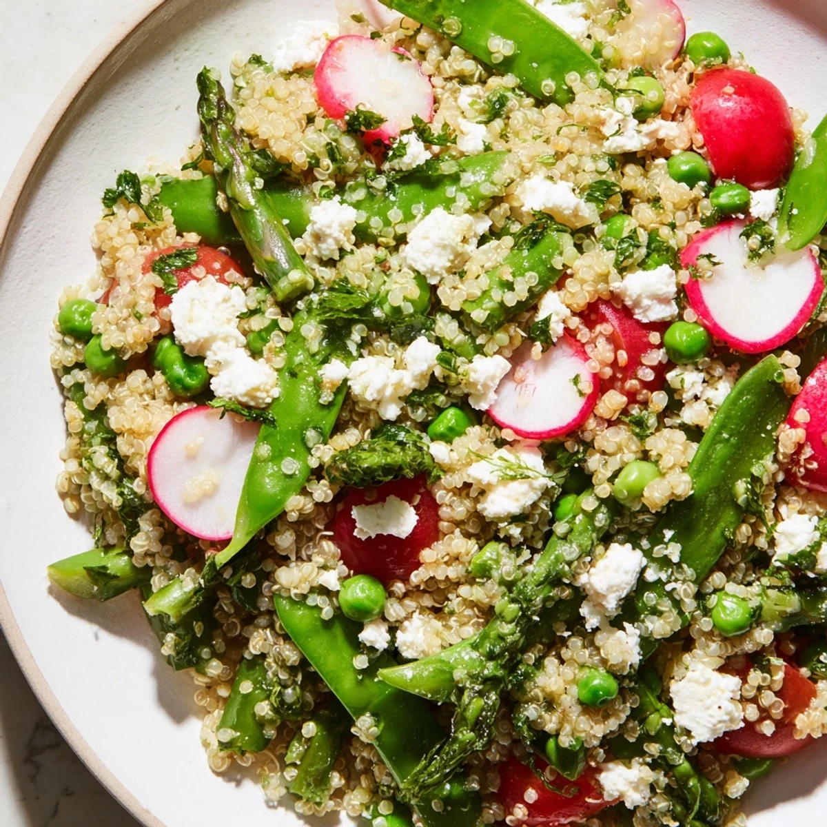 Spring vegetable quinoa salad in a white bowl with fresh herbs and crumbled feta on top