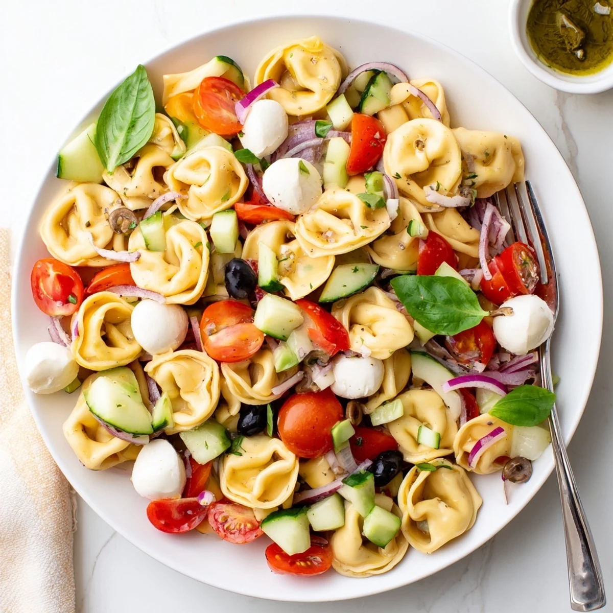 Chilled tortellini salad served in a white bowl with fresh basil and crisp vegetables