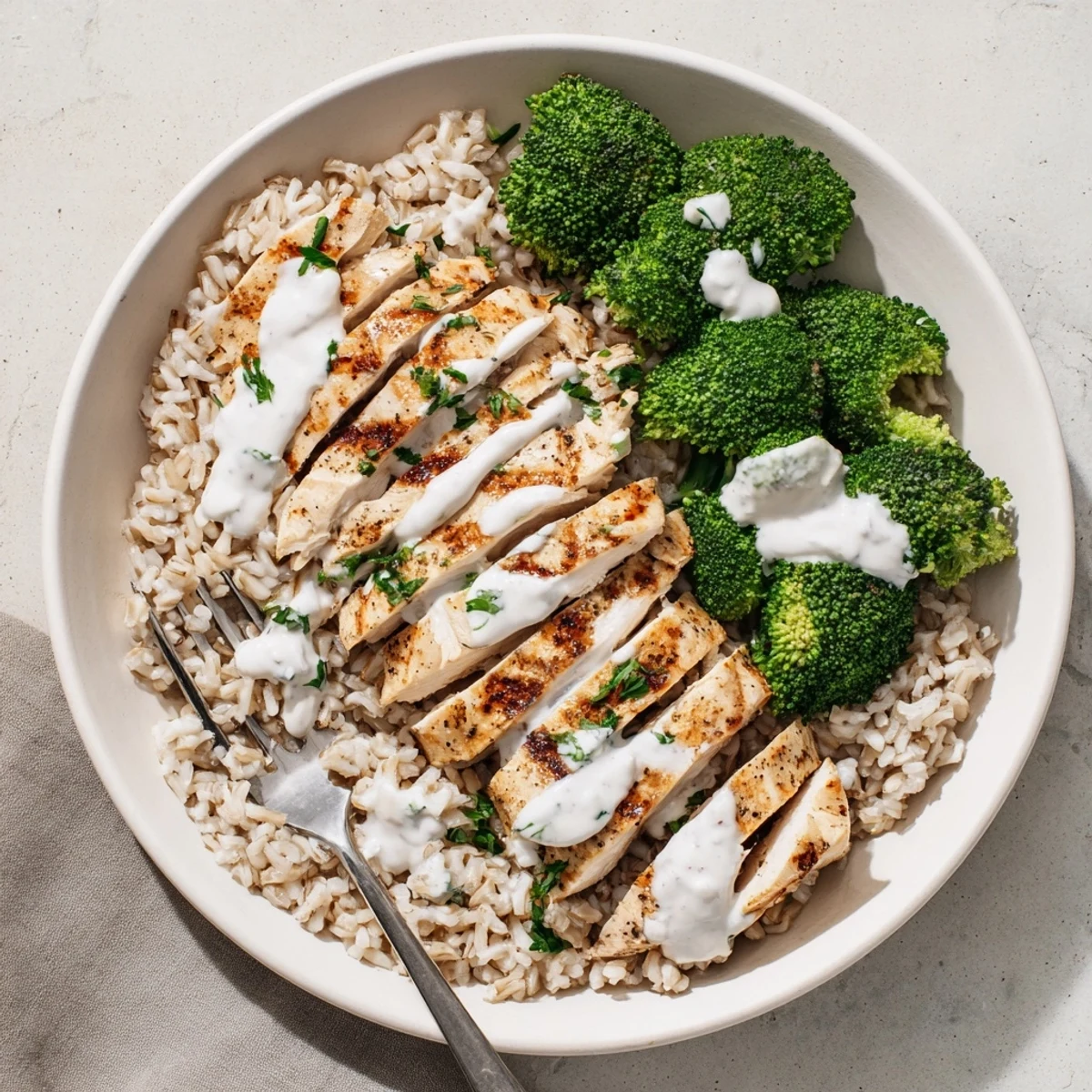 Golden grilled chicken slices and vibrant steamed broccoli drizzled with rich garlic yogurt sauce in a wholesome bowl.