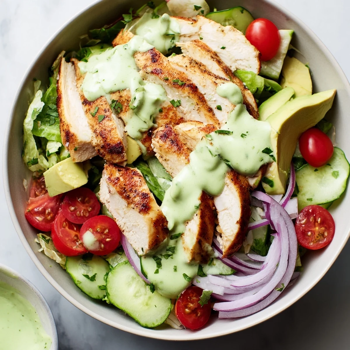 Colorful bowl with grilled chicken strips, fresh avocado, crisp vegetables, and creamy green dressing