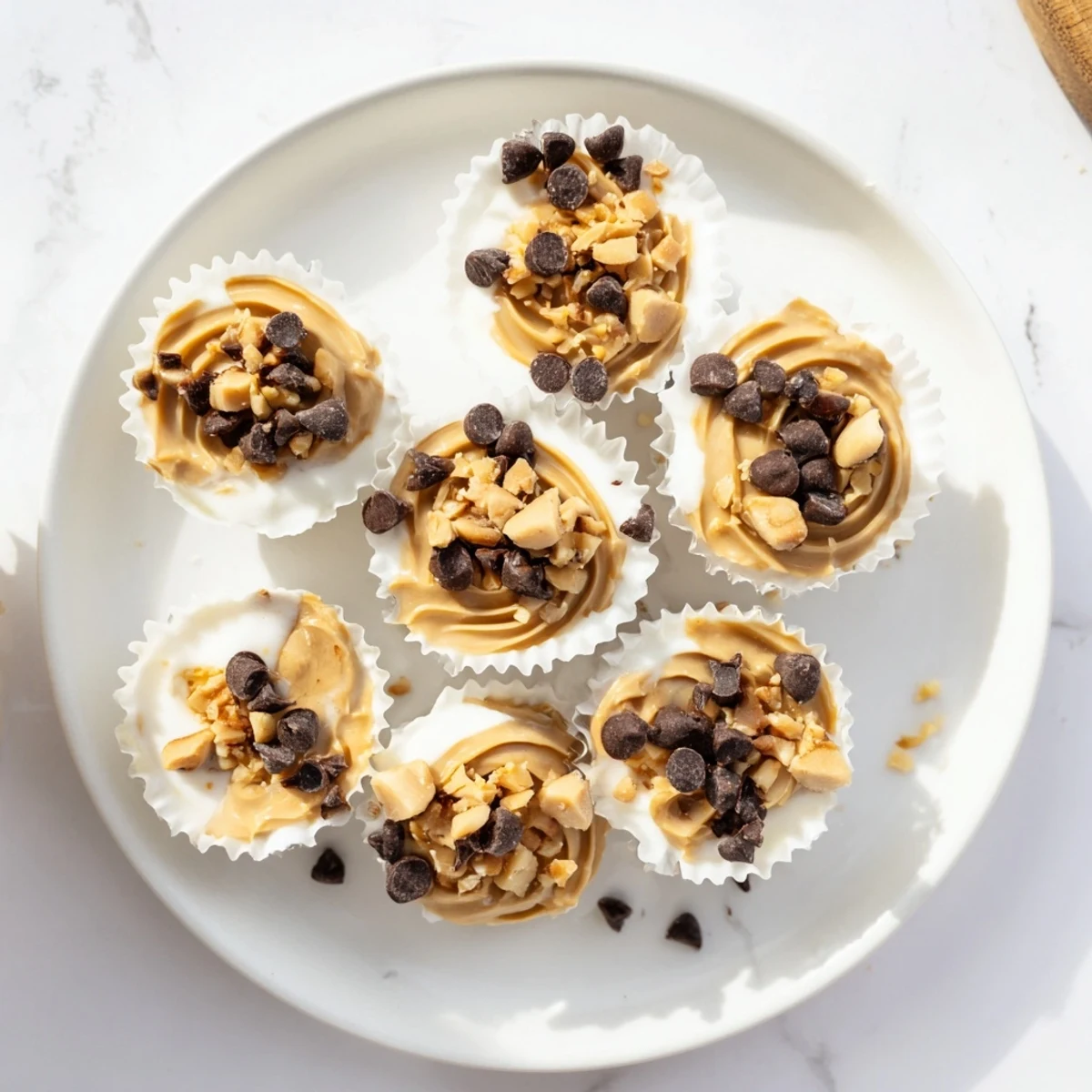 Creamy frozen peanut butter Greek yogurt bites topped with melted chocolate chips and chopped peanuts in a mini muffin tin