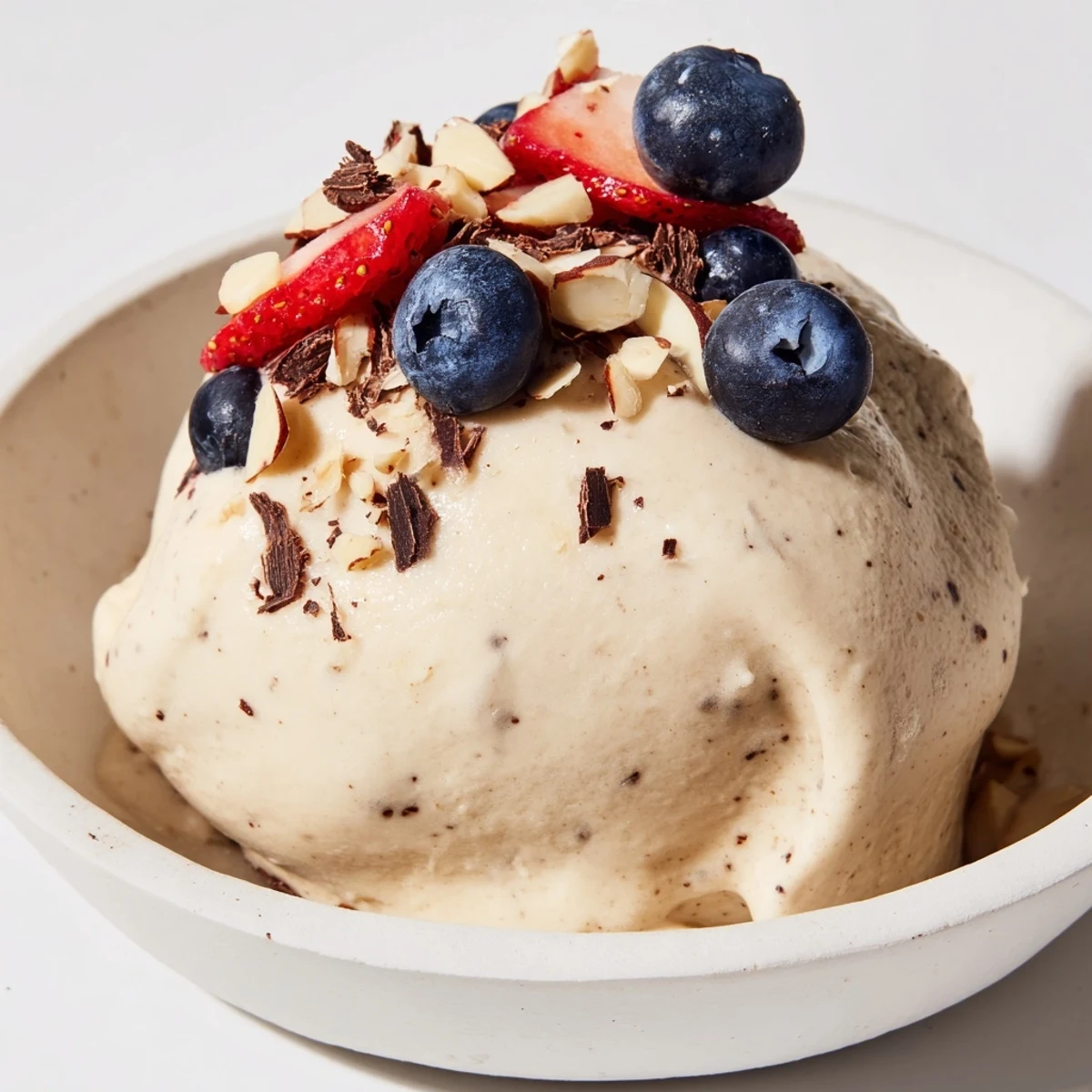 Creamy banana nice cream topped with fresh berries and dark chocolate chips in a white bowl