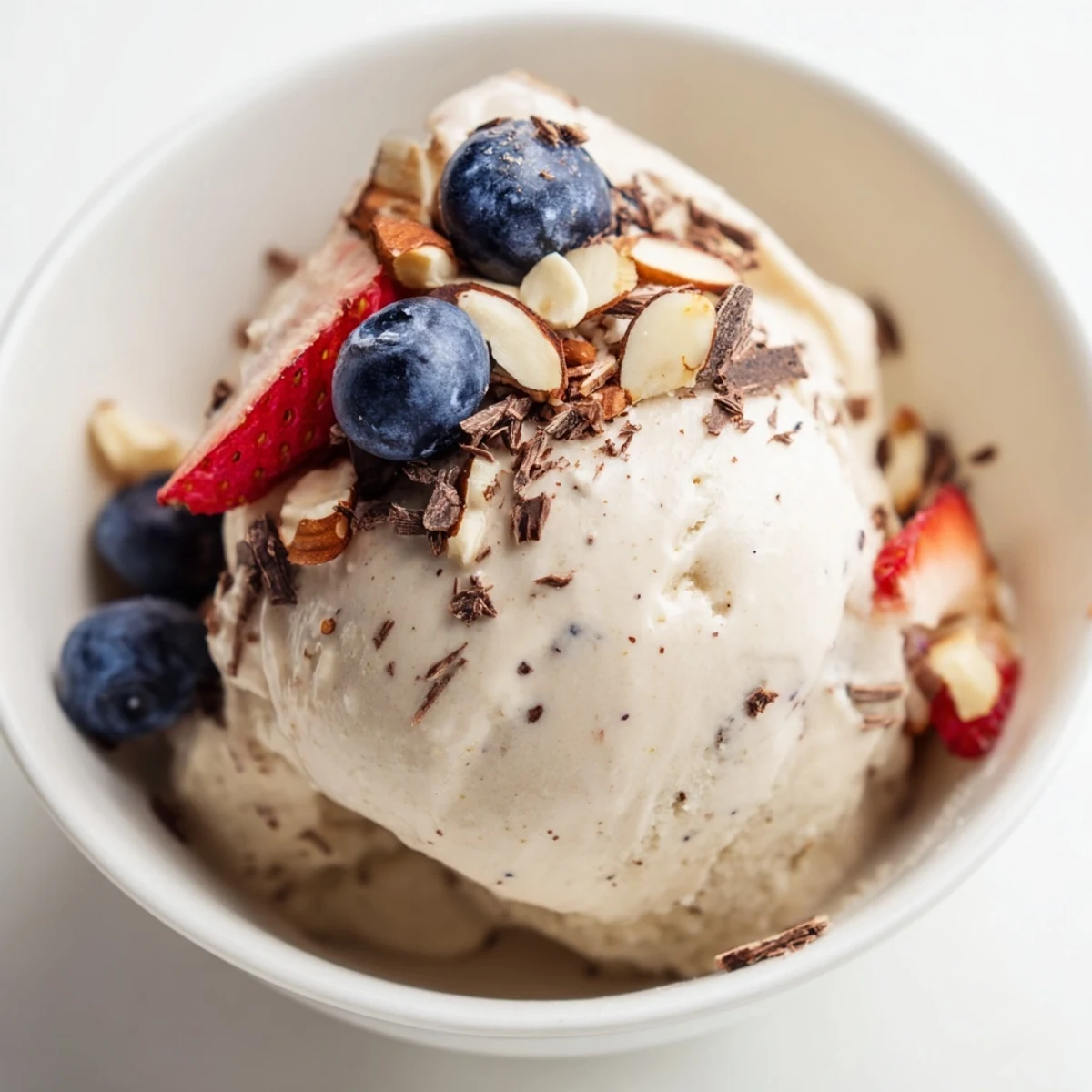 Smooth dairy-free banana nice cream with chopped nuts and fresh fruit garnish on a marble background