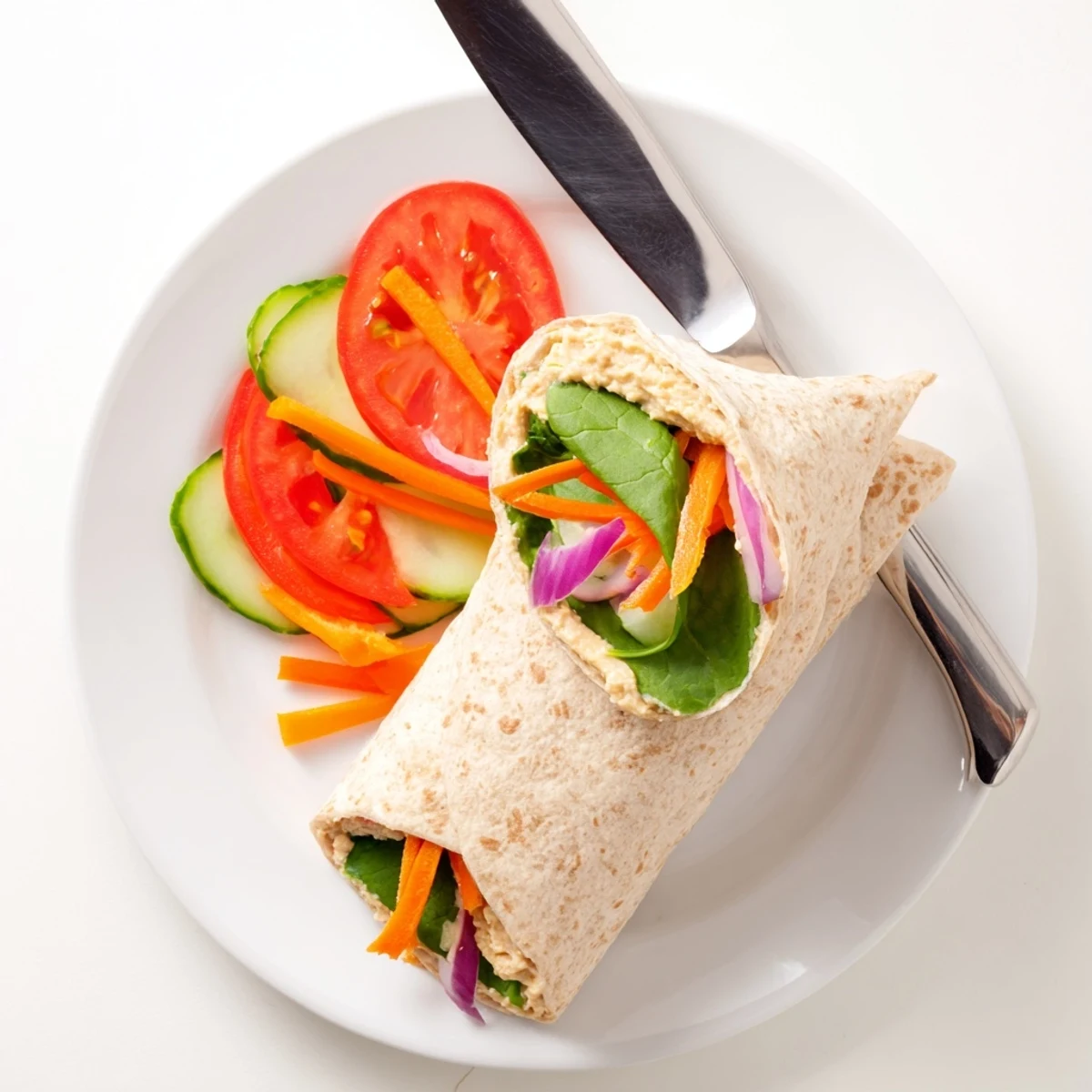 Golden whole wheat tortilla wrapped around creamy hummus and crisp colorful fresh vegetables