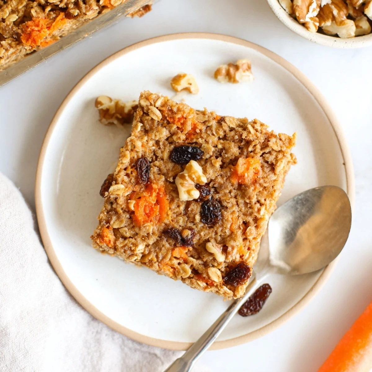 Golden carrot cake baked oatmeal sprinkled with chopped walnuts and raisins in a square baking dish