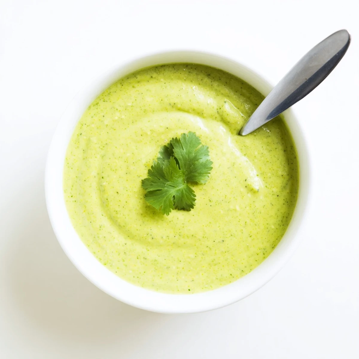 Small bowl of spicy Peruvian aji verde sauce topped with fresh cilantro leaves and lime