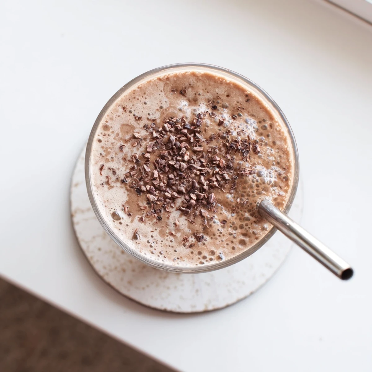 Glass of frothy raw chocolate banana shake garnished with coconut flakes and banana slices