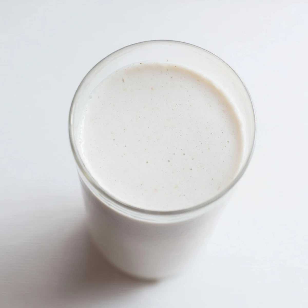 Glass of homemade almond milk on a wooden table with spilled raw almonds alongside