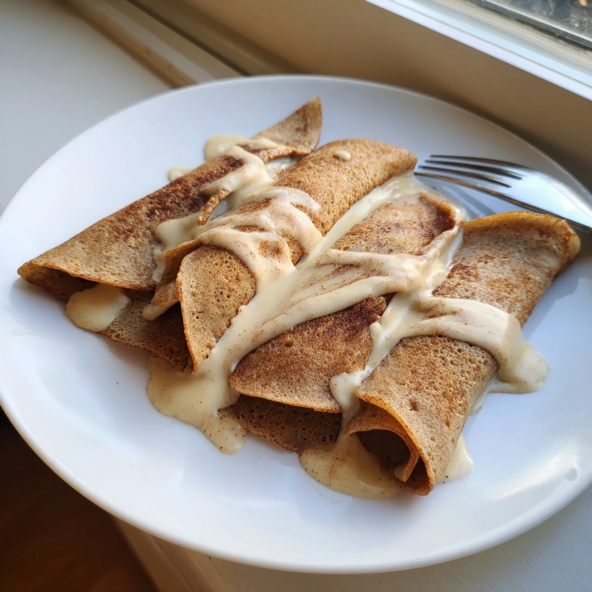 Golden cinnamon roll protein crepes drizzled with sweet cream cheese glaze on a white plate