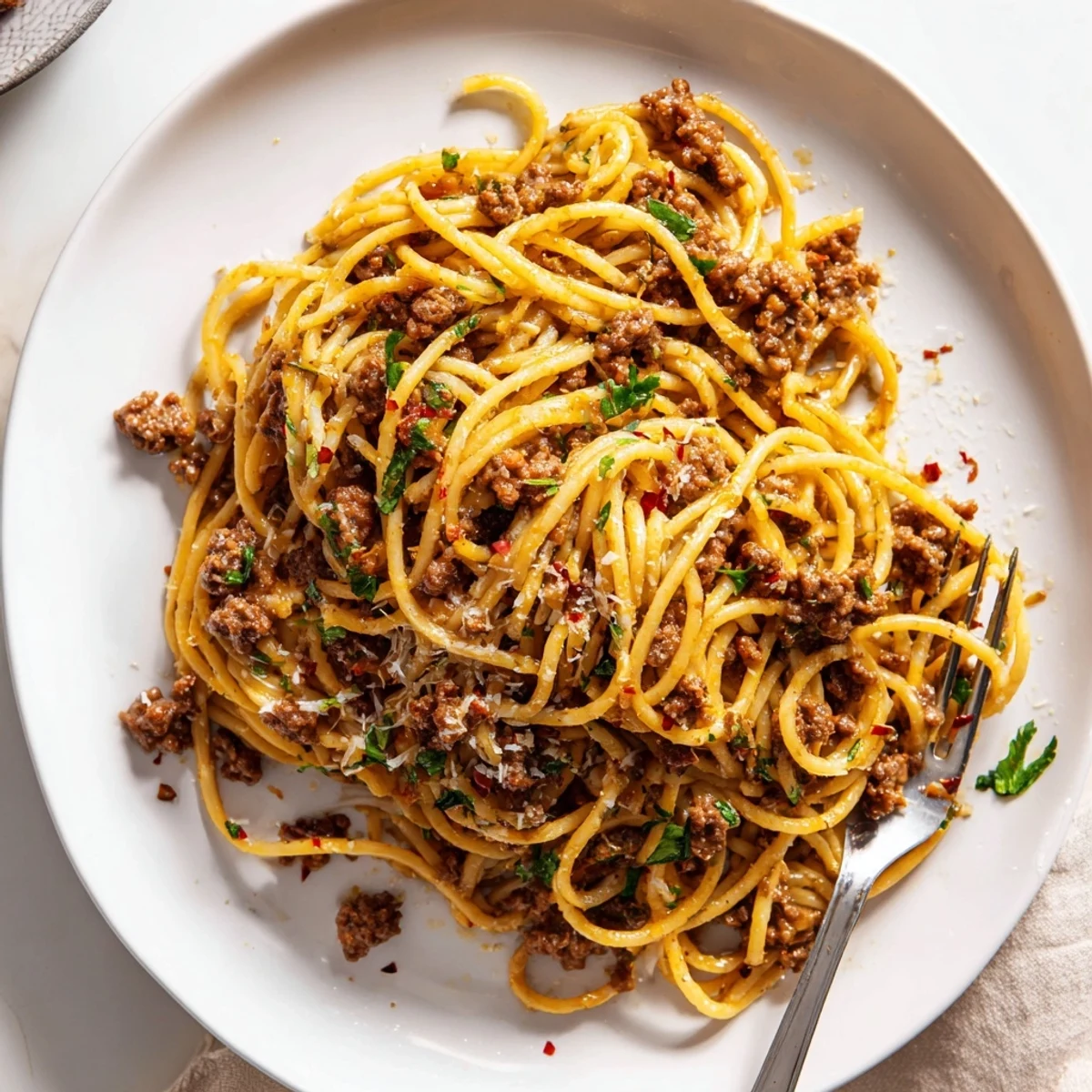Steaming plate of garlic butter pasta with ground beef coated in a golden, savory sauce