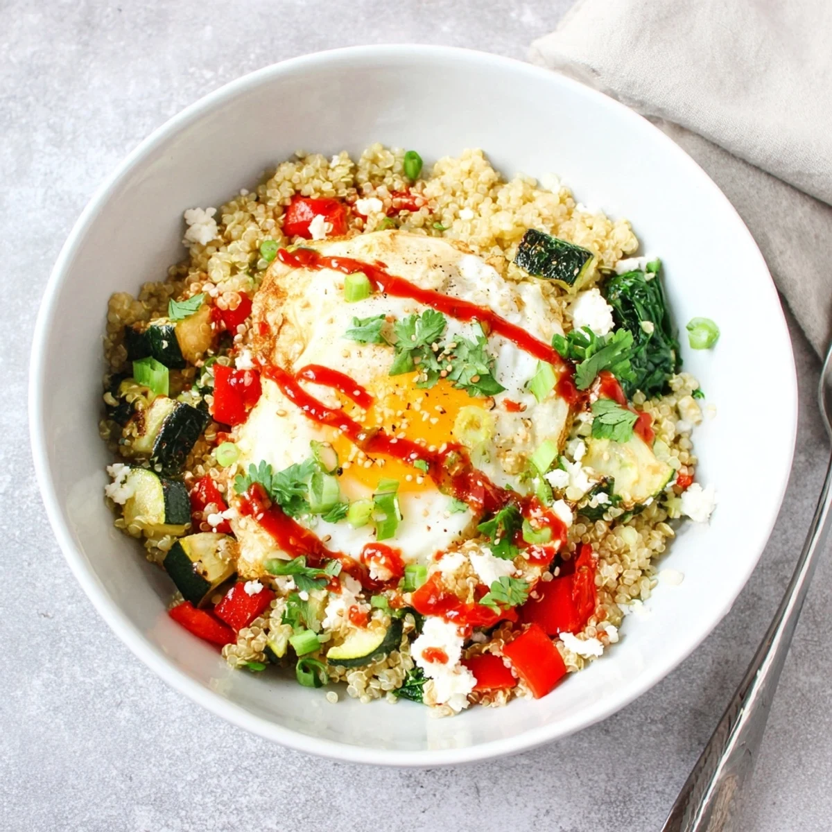 Savory quinoa breakfast bowl topped with a runny egg and colorful sautéed vegetables