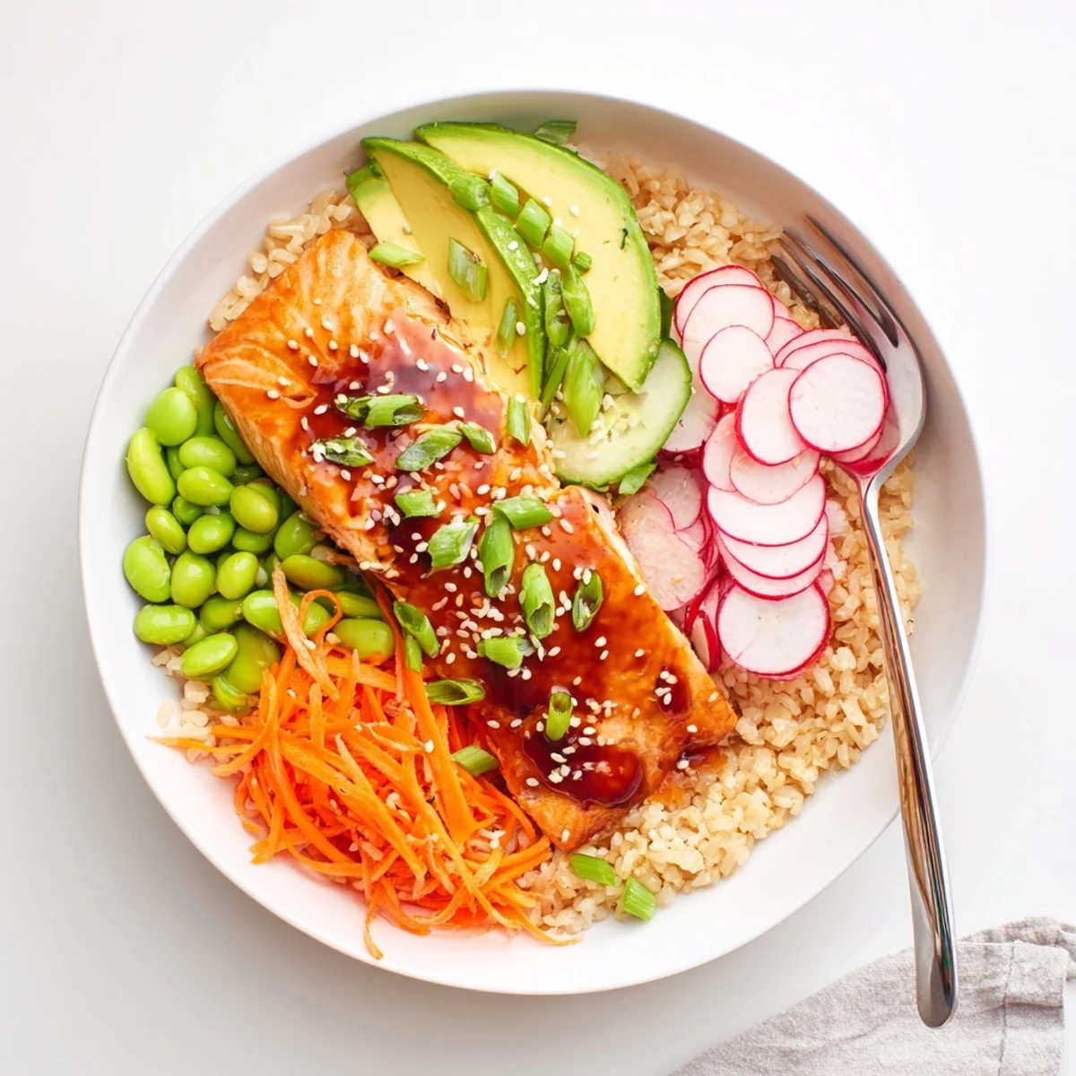 Tender caramelized salmon over warm grains surrounded by vibrant shredded carrots and edamame