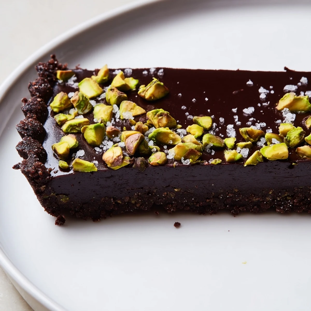 Rich Dark Chocolate Pistachio Tart sliced into neat wedges on a rustic wooden serving board