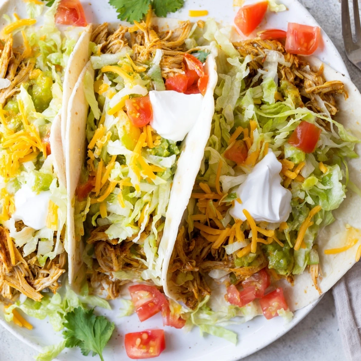 Shredded slow cooker ranch chicken tacos served in warm tortillas with sour cream