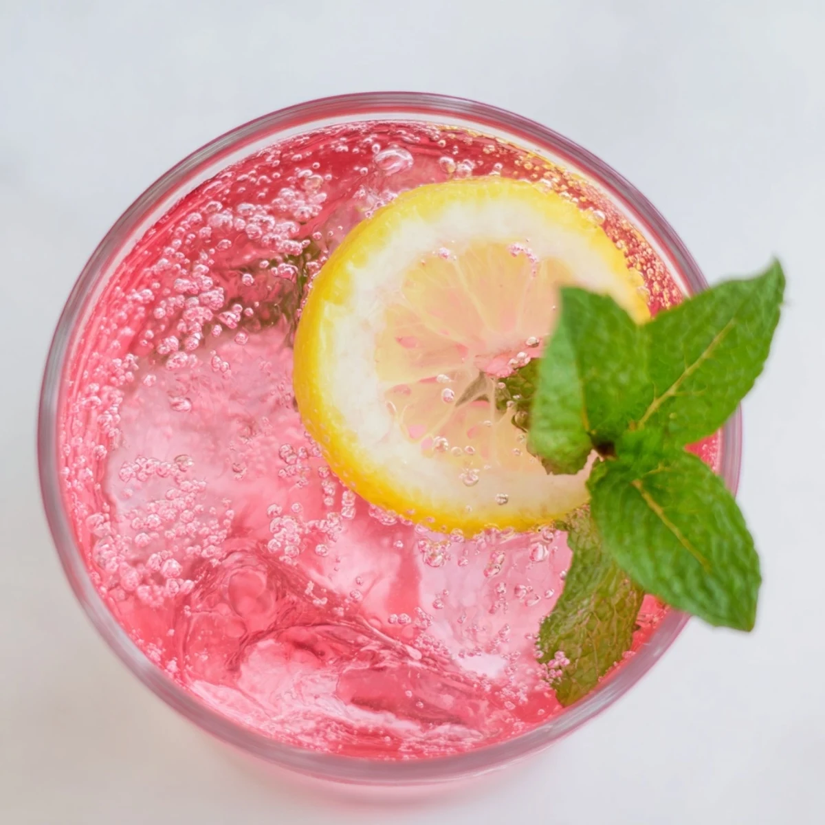Sparkling Honey Lemon Pink Soda in a tall glass garnished with raspberries and mint