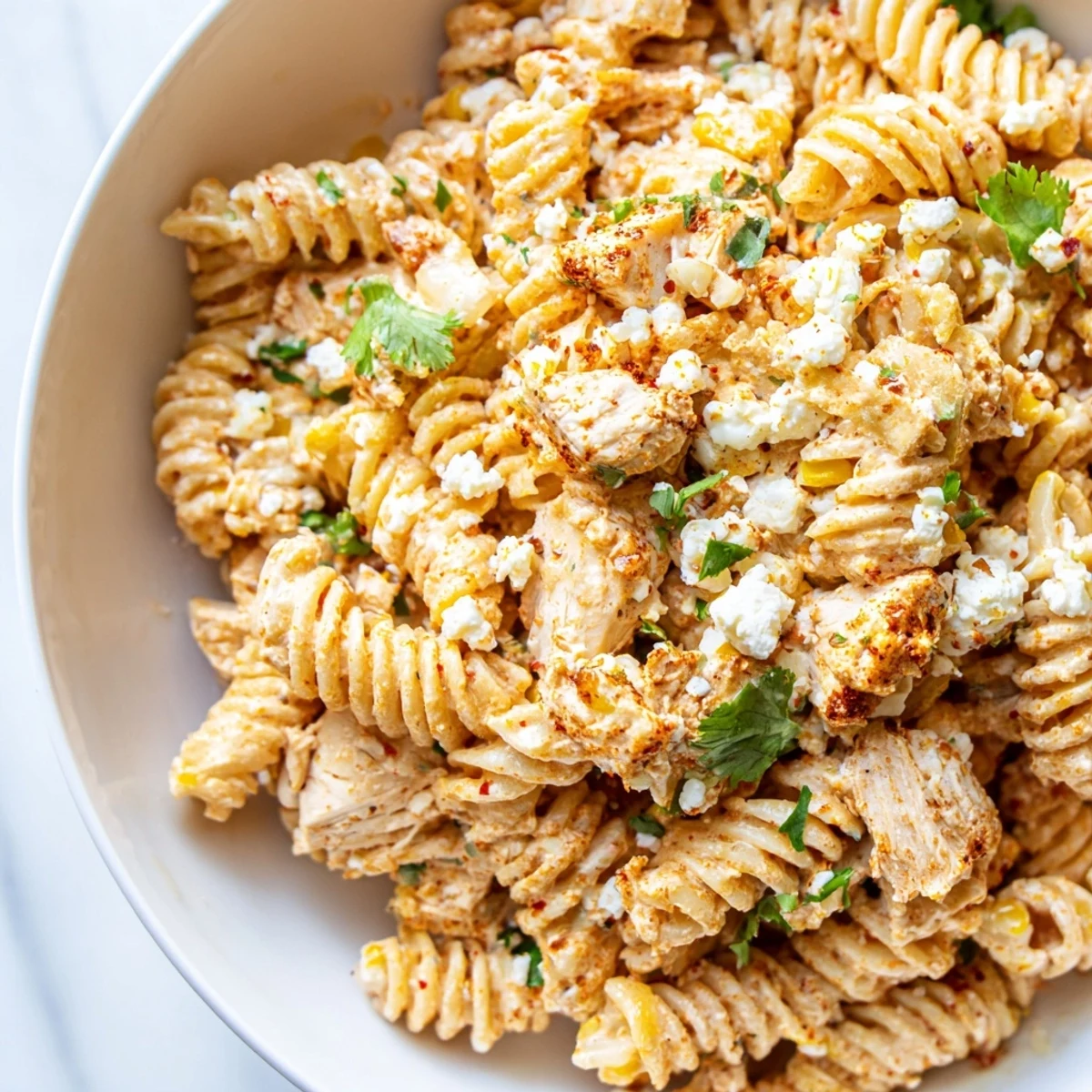 Colorful elote style chicken pasta salad in a large bowl with charred corn kernels and fresh cilantro garnish.