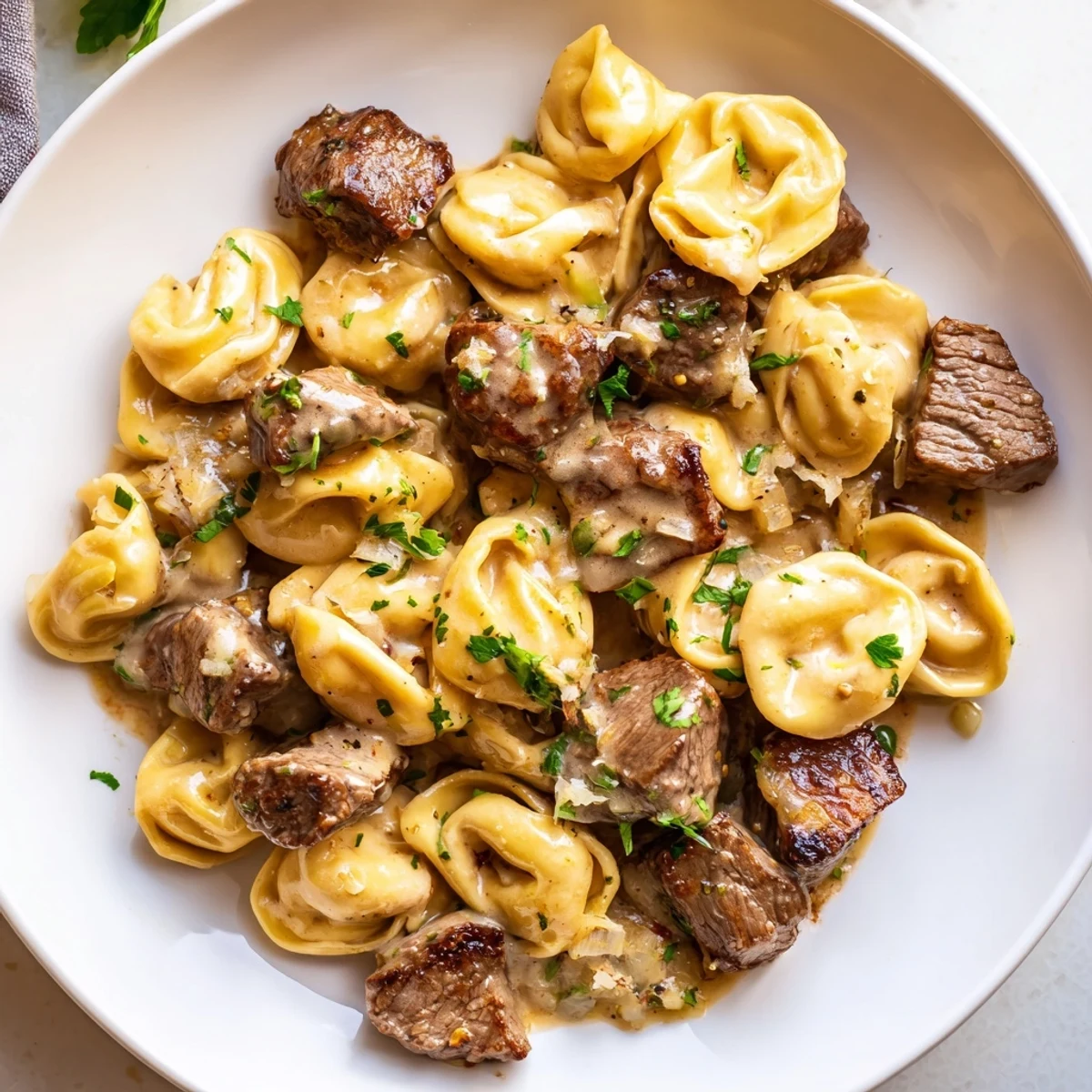 Creamy garlic steak tortellini served in a white bowl with fresh parsley sprinkled on top