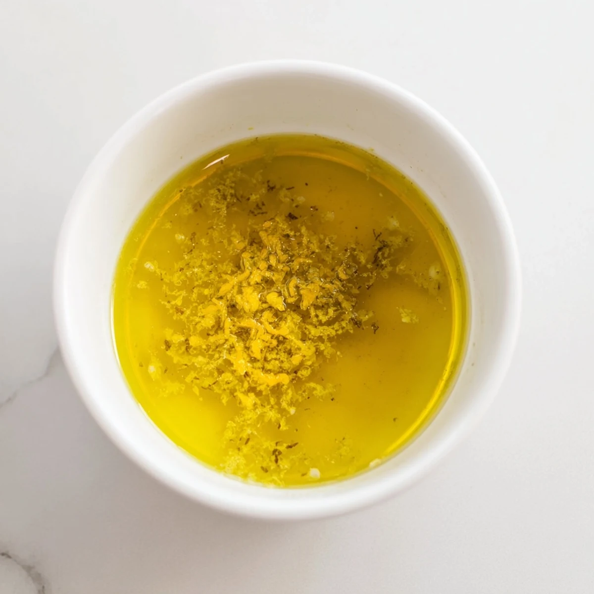 Bright lemon vinaigrette dressing recipe whisked in a bowl with lemon zest and garlic.