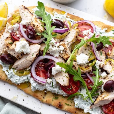 Golden-baked Zesty Lemon Herb Chicken Flatbread With Creamy Feta features arugula, cherry tomatoes, and a drizzle of extra virgin olive oil.