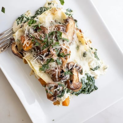 Butternut Squash, Spinach & Mushroom Lasagna baked in a white ceramic dish with fresh basil garnish.