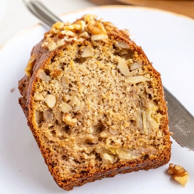 Warm slice of Nana's Secret Banana Nut Bread drizzled with butter on a ceramic plate