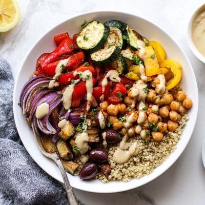 A warm vegan Mediterranean roasted vegetables bowl served over quinoa with kalamata olives and fresh parsley garnish.